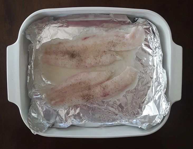 Rockfish fillets in baking dish after seasoning and lemon butter added